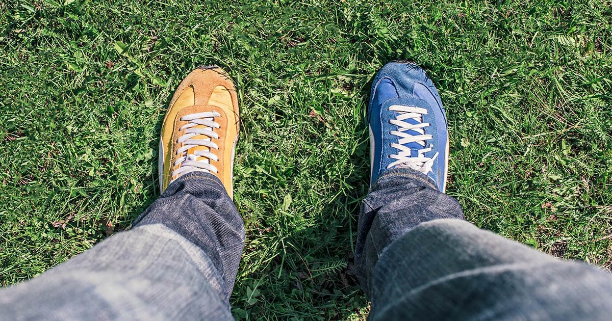 Man wearing one yellow shoe and one blue shoe