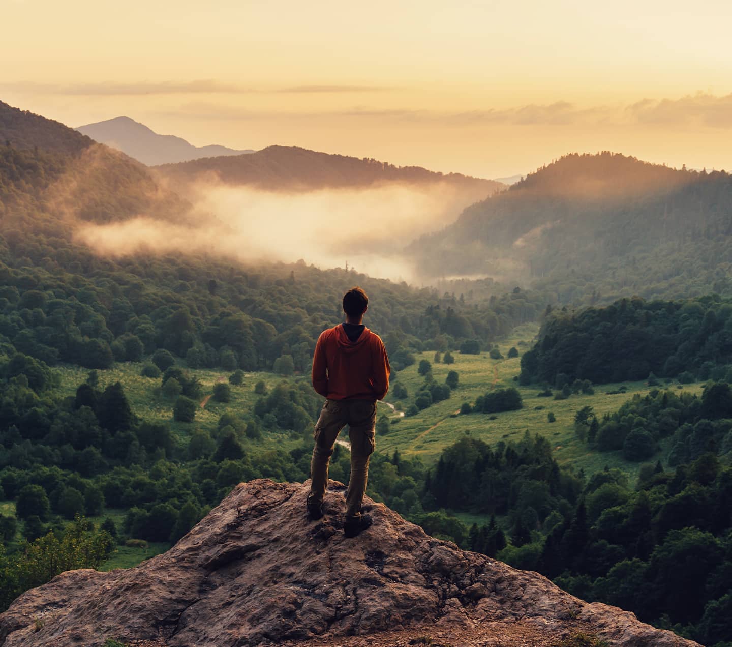 Man exploring and standing on top of cliff at sunset