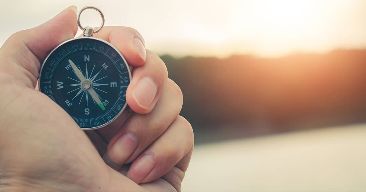 Compass on a mountain at sunset sky.