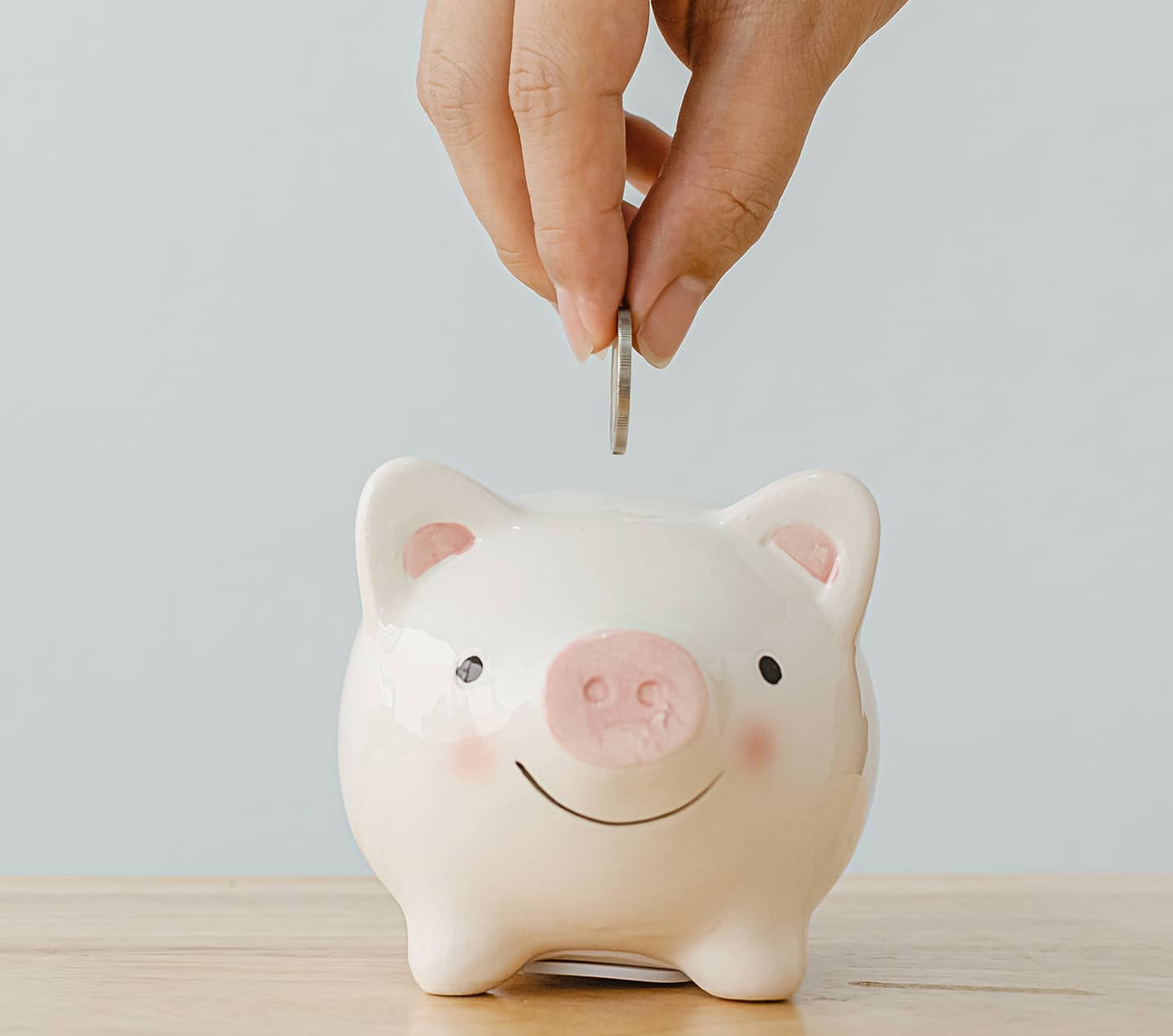 A hand putting coins in a piggy bank