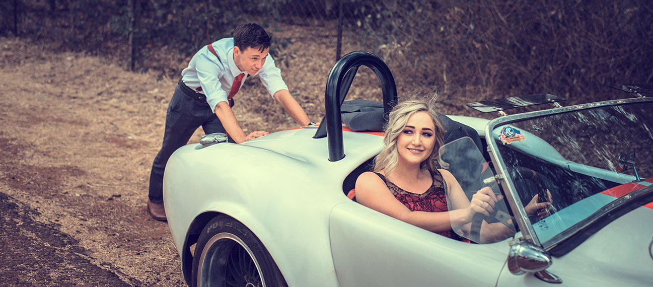 Woman sitting on a car while man is pushing it