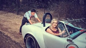 Woman sitting on a car while man is pushing it